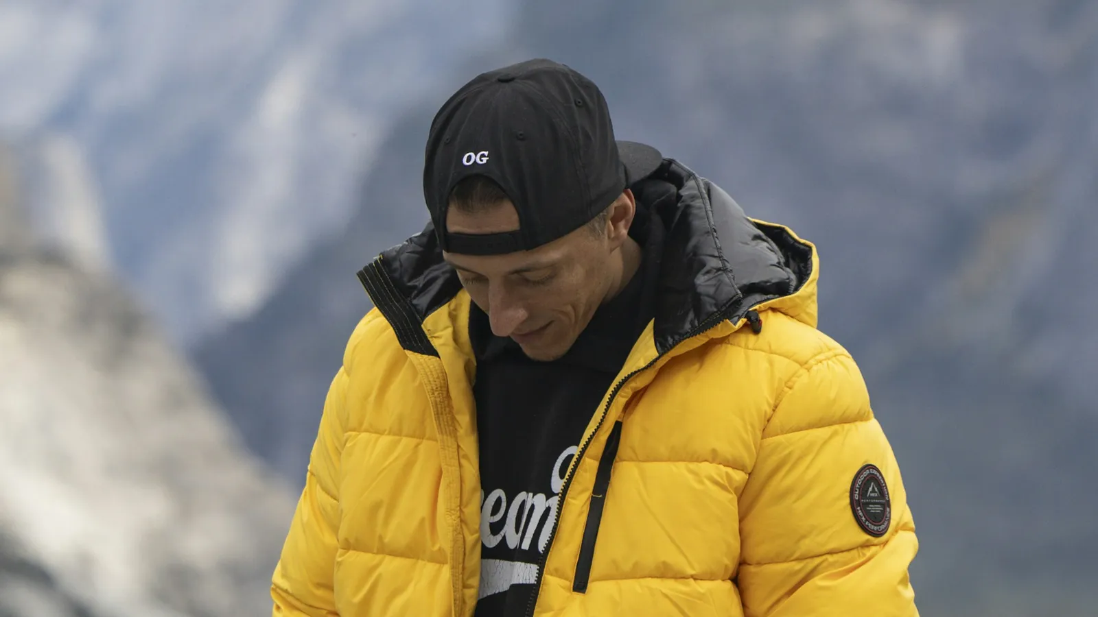Hiker in a yellow insulated jacket with mountains behind