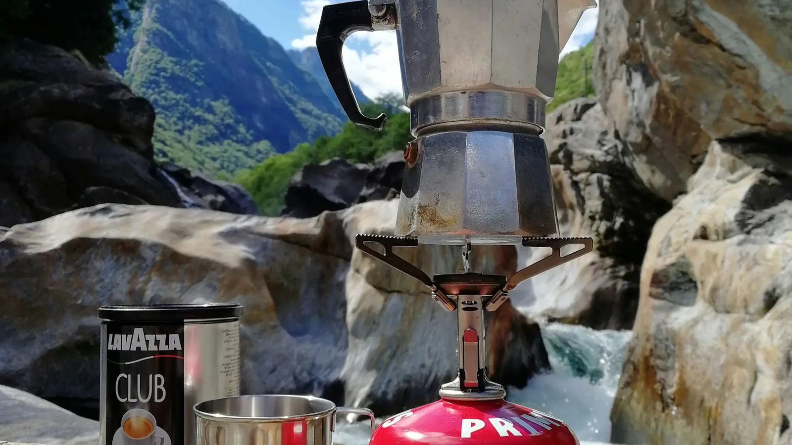 Single-burner camp stove brewing coffee on a riverside rock