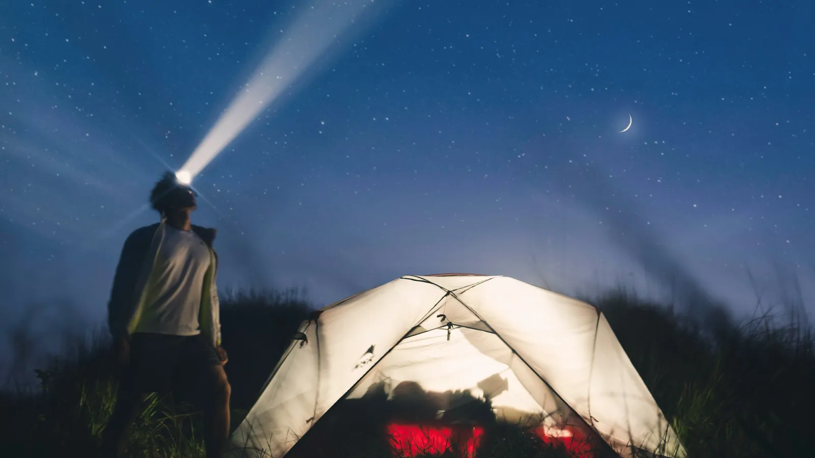 Camper wearing a headlamp in front of a tent at night