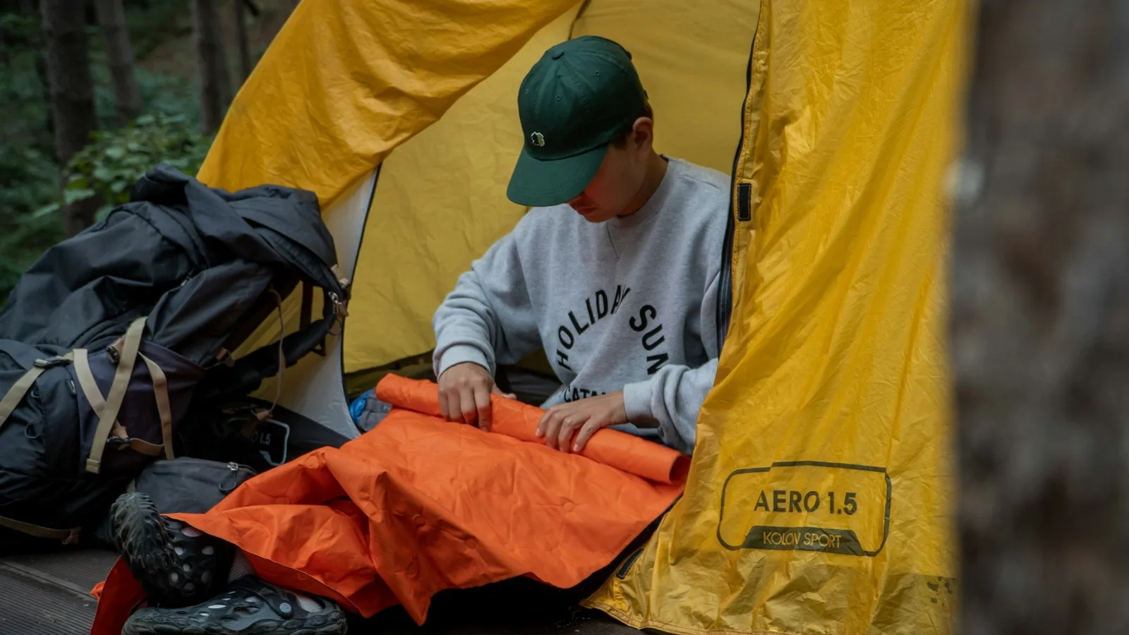 Camper sitting inside a tent next to an unrolled sleeping bag