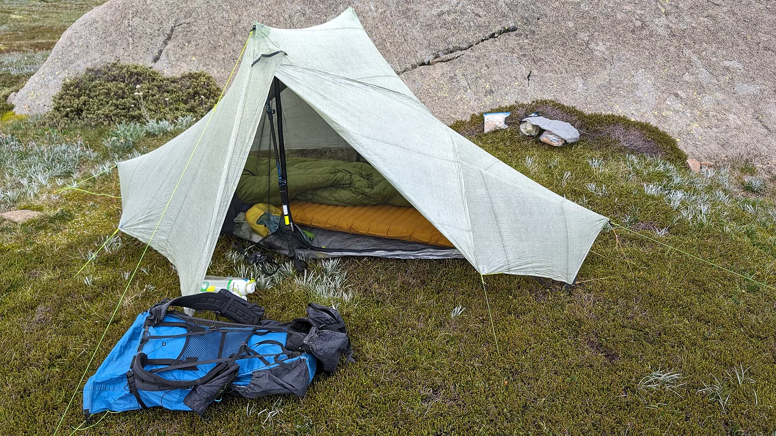 Sleeping bag beside a tent and backpack at a campsite